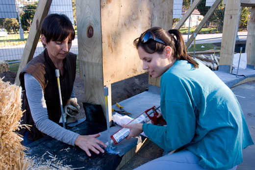 A mother and daughter team apply silicon sealant in peparation for placing the straw bales.